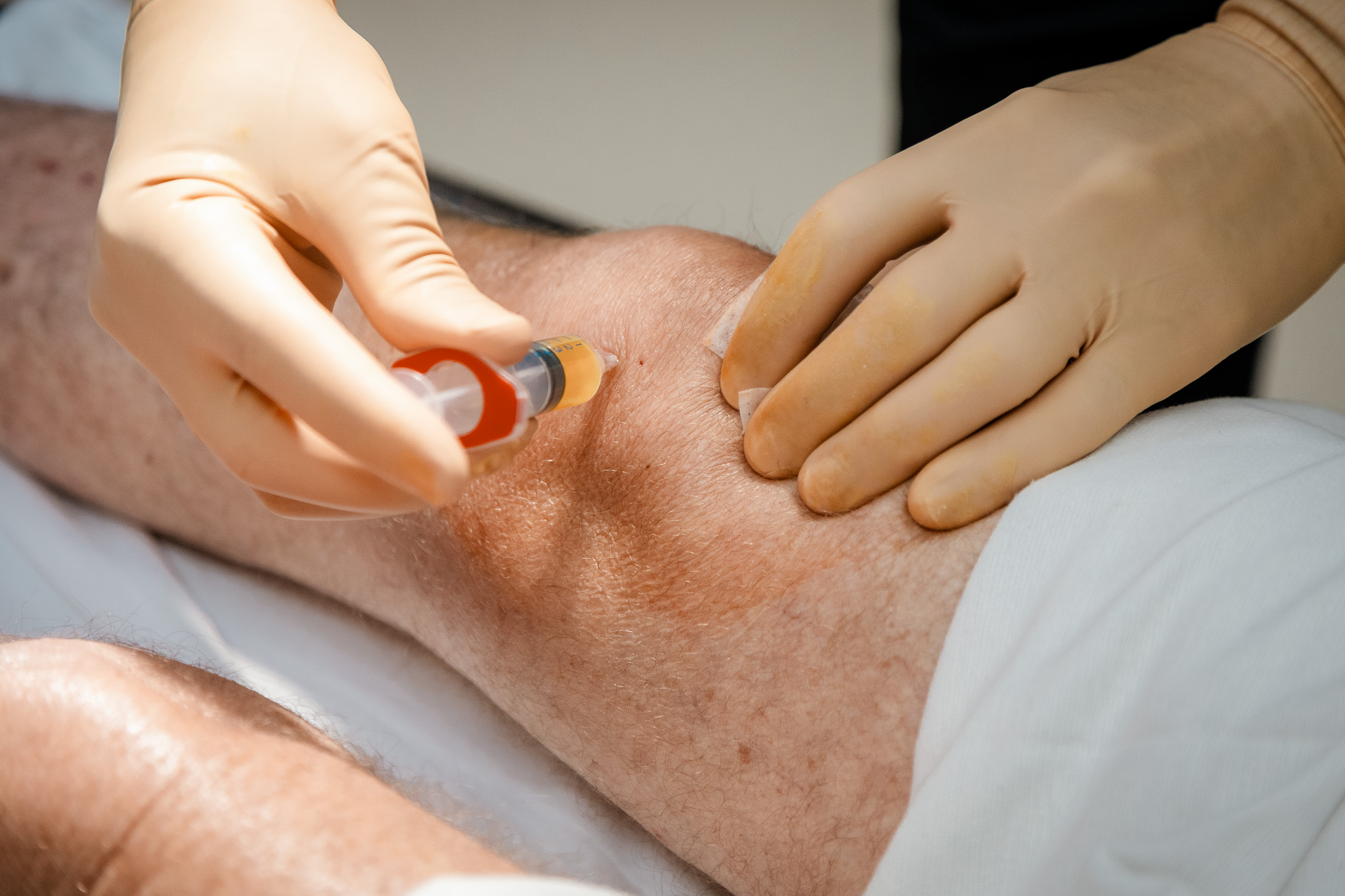A gloved injection into a patient's knee